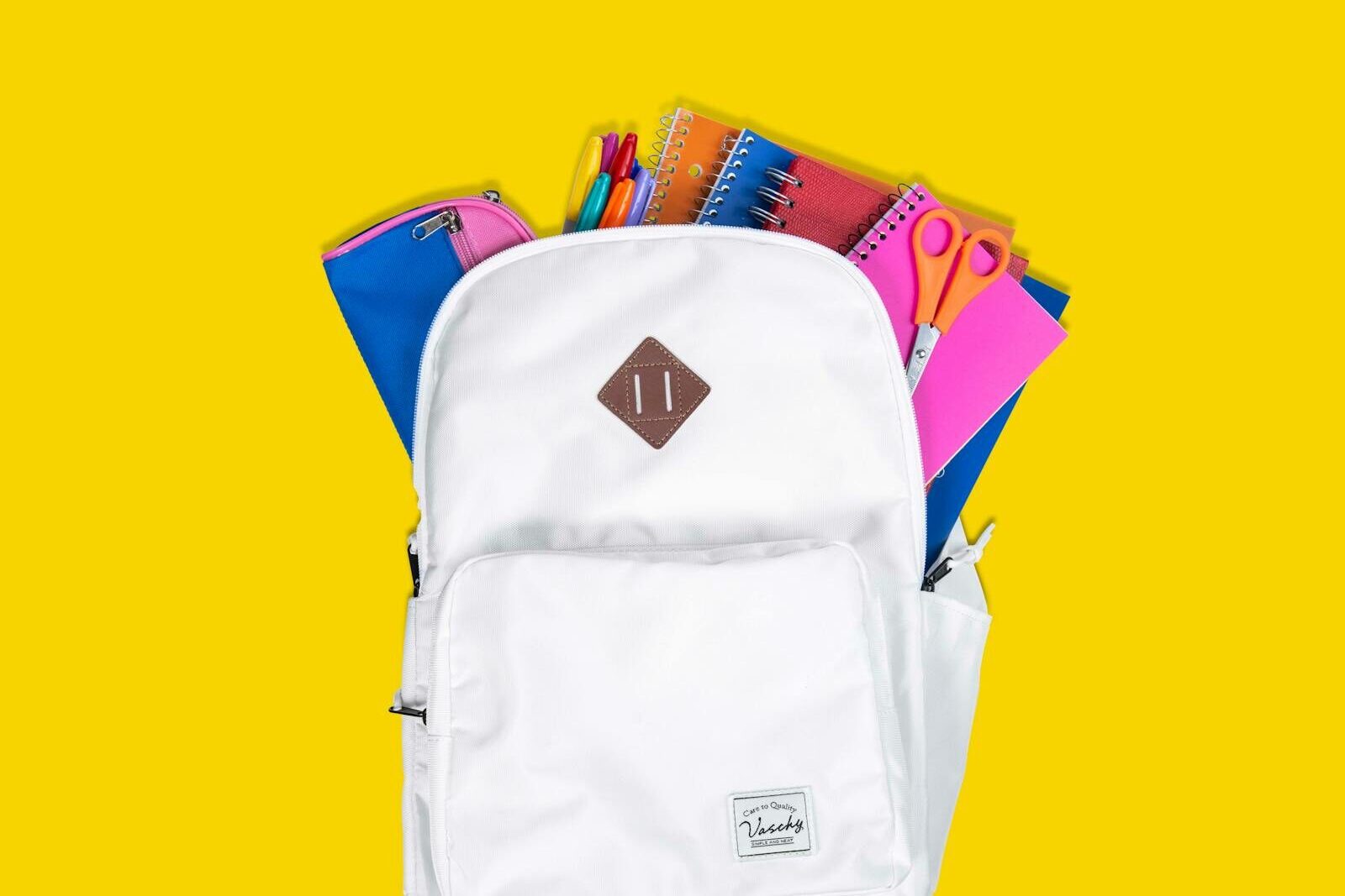 Colorful school supplies in a white backpack against a vibrant yellow background.