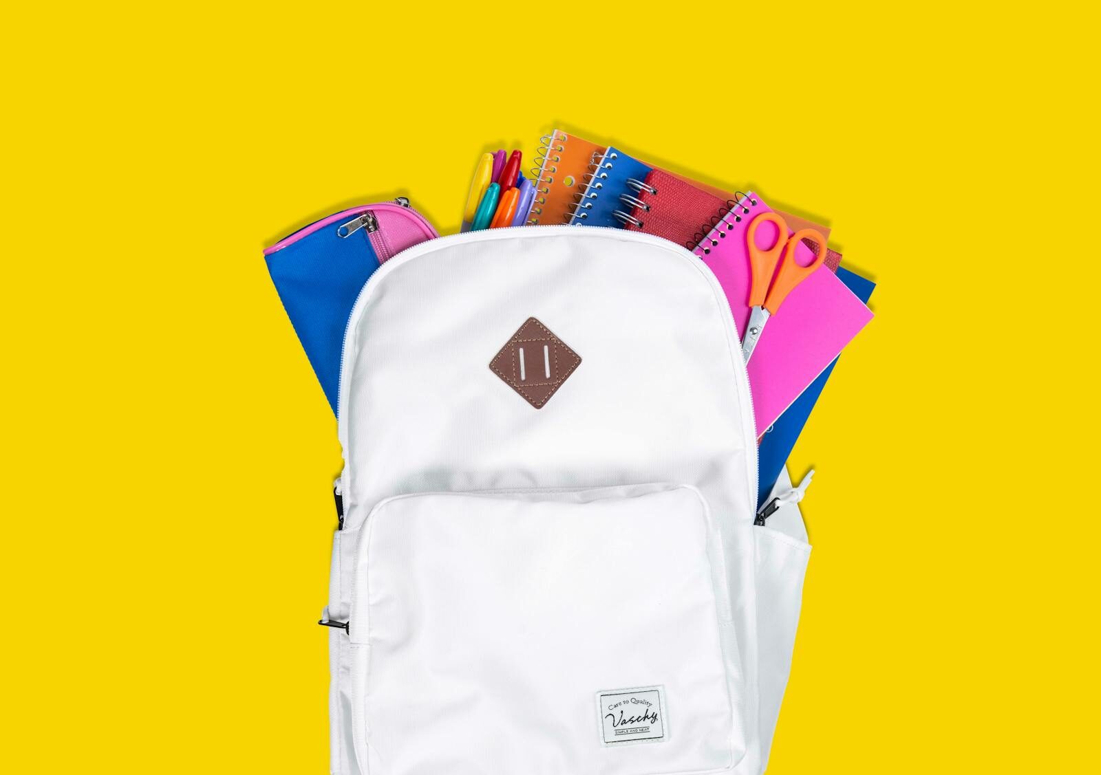 Colorful school supplies in a white backpack against a vibrant yellow background.