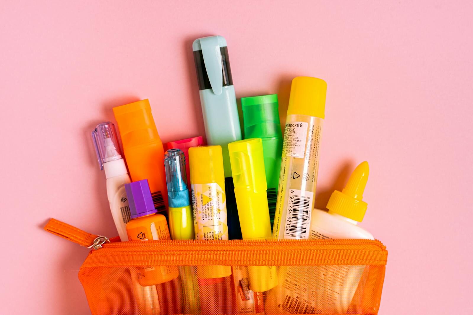 Bright office essentials in a mesh pouch on a pink background. Perfect for stationery enthusiasts.